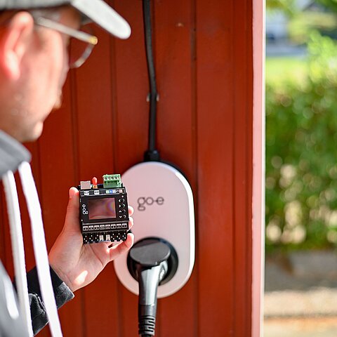 go-e Controller wird vor einem go-e Charger Gemini gehalten